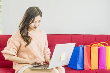 Güzel kadın kırmızı Kanepede oturan, renkli kağıt alışveriş çantası