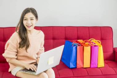 Güzel kadın kırmızı Kanepede oturan, renkli kağıt alışveriş çantası