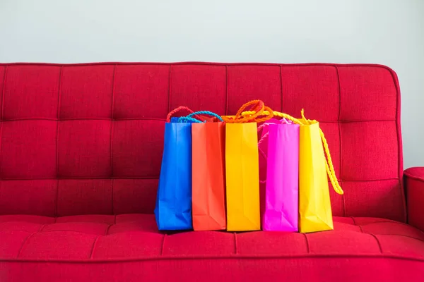 Bolsas de papel de compras coloridas colocadas en un sofá rojo y paredes blancas — Foto de Stock