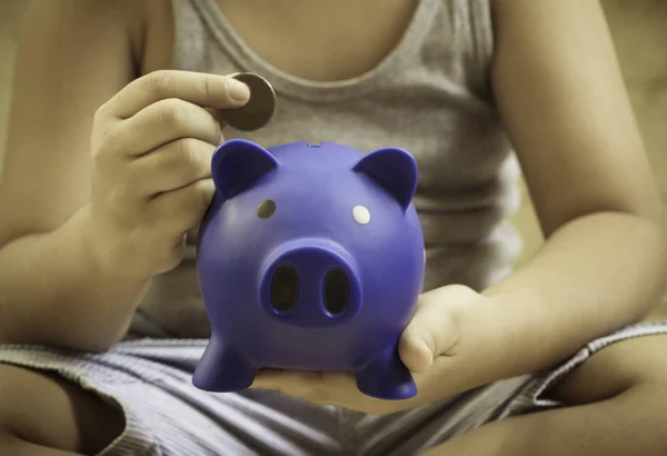 Little boy sitting, saving blue piggy bank in hand, concept of f
