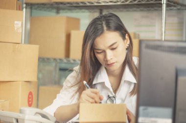 Ev ofisi ve küçük işletme sahibi iş kadını girişimi, paketli teslimat paketi, karton kutu ve müşterileri çevrimiçi siparişlerden e-ticaret şirketlerine teslim etmek için yazma adresleri