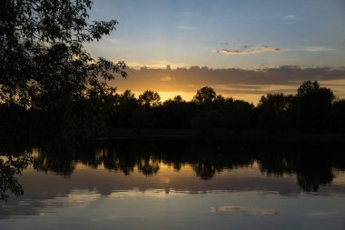 Bir yaz akşamı gölün kıyısında inanılmaz inanılmaz çok renkli gün batımı. Bulutlar suya yansıyor..
