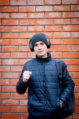 Genç bir adam bir tuğla duvara yaslanmış duran ve kulaklık müzik dinle.