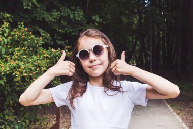 sevimli gülümseyen kız ormanda ortaya iki parmak, her şey yolunda.