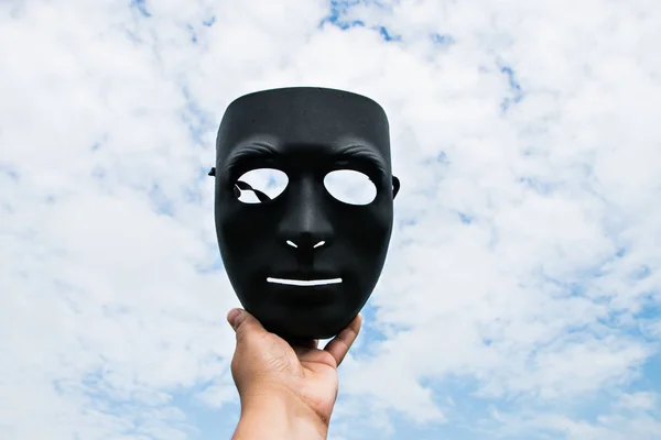 black plastic mask on blue sky background in hand.