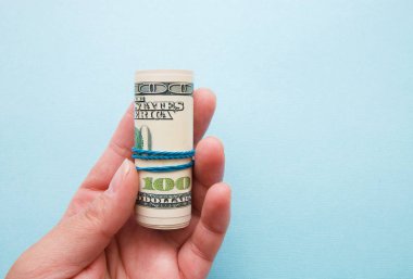 mavi bir arka plan üzerinde bir kadının elinde bir boru içine haddelenmiş Doları para.