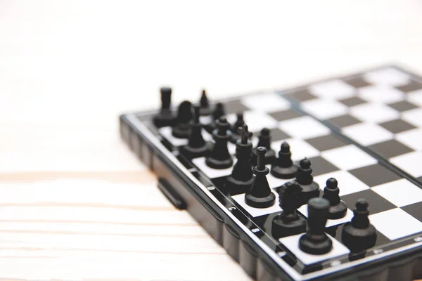 Piccoli scacchi tascabili, pezzi di scacchi di plastica posti su una scacchiera su uno sfondo di legno bianco — Foto Stock