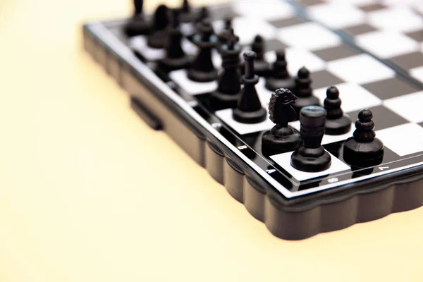 Small pocket chess, plastic chess pieces placed on a chessboard on a yellow background — Stock Photo, Image