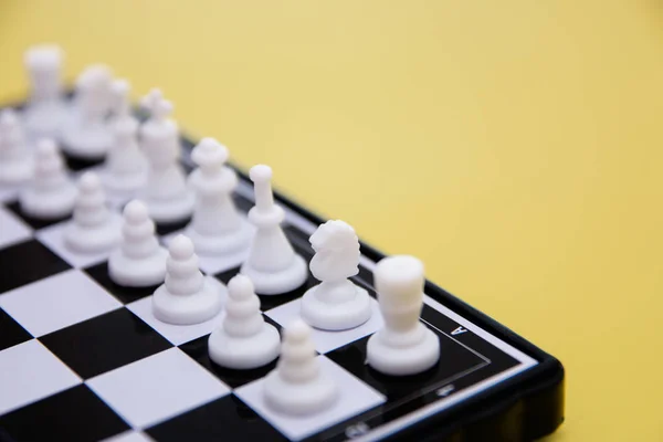 Piccoli scacchi tascabili, pezzi di scacchi di plastica posti su una scacchiera su fondo giallo — Foto Stock