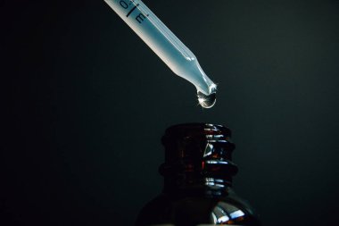 Bir damla bir pipet homeopatik ilaç, karanlık bir arka plan yakın çekim bir şişe içine düşüyor.