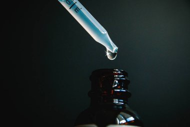 Bir damla bir pipet homeopatik ilaç, karanlık bir arka plan yakın çekim bir şişe içine düşüyor.