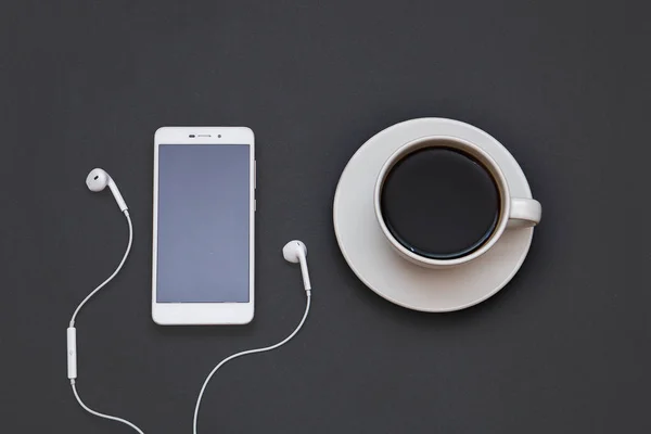 Auscultadores, telemóvel e uma chávena de café num fundo preto. Conceito musical. Vista superior com espaço de cópia — Fotografia de Stock