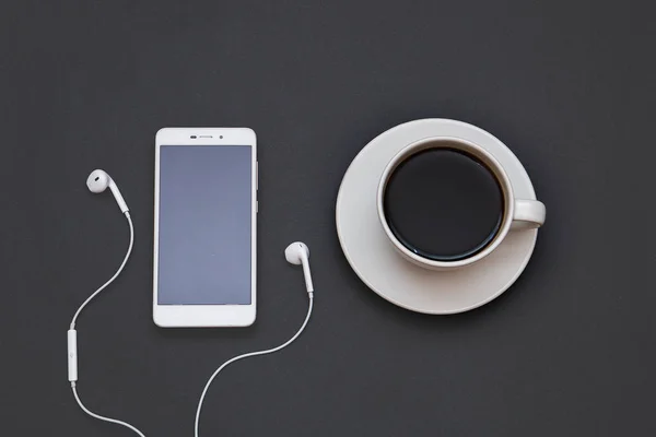 Headphones, mobile and a Cup of coffee on a black background. Musical concept. Top view with copy space
