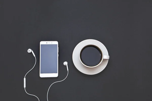 Headphones, mobile and a Cup of coffee on a black background. Musical concept. Top view with copy space