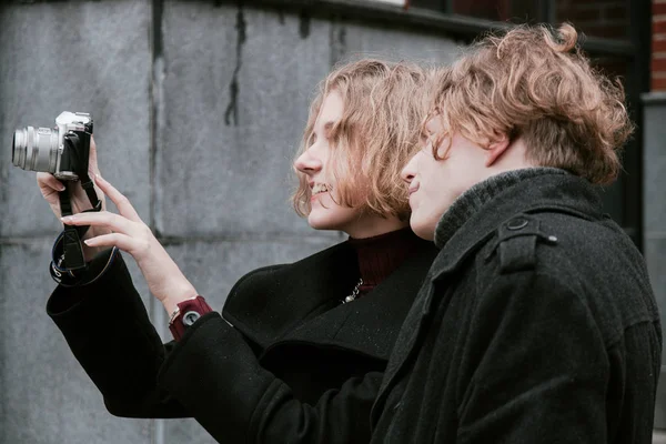 Blond curly-haired guy and the same girl take pictures of themselves and take pictures around — Stock Photo, Image