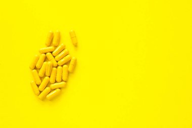 Sarı arka plan üzerinde izole sarı kapsüller, metin için boşaltmak, seçici odak, üst görünüm. İlaç istismarı kavramının tedavisi için ağrı ilaçları, sağlık, haplar