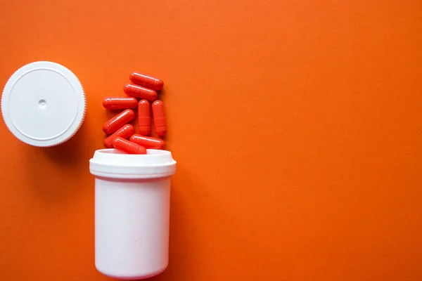 Orange capsules from a white bottle on an orange background. copyspace for text, selective focus, top view. Pain meds, health, pills for the treatment of the concept of drug abuse