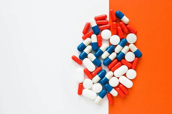 Multicolored capsules isolated two white and orange background, copyspace for text, selective focus, top view. Pain meds, health, pills for the treatment of the concept of drug abuse