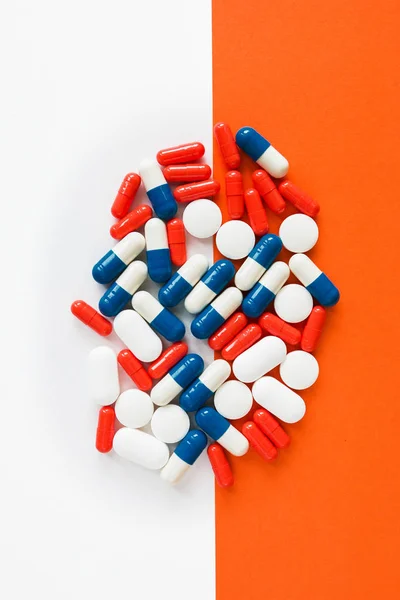 Multicolored capsules isolated two white and orange background, copyspace for text, selective focus, top view. Pain meds, health, pills for the treatment of the concept of drug abuse