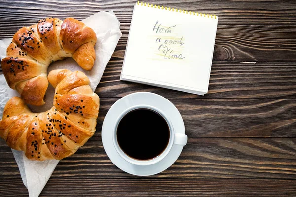 Uma xícara de café instantâneo com um croissant e mensagem ter um bom tempo no fundo de madeira texturizada vista superior, café da manhã acolhedor e delicioso — Fotografia de Stock