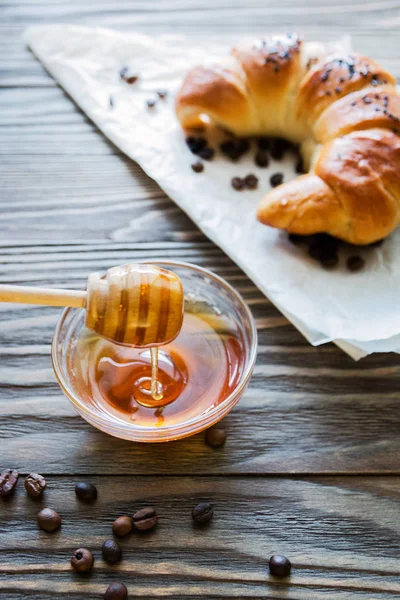 Croissant, mel e grãos de café em um fundo de madeira texturizado vista superior, aconchegante e delicioso café da manhã. Fundo rústico — Fotografia de Stock