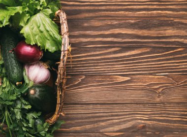 Organik ürünler, taze sebzeler içeren küçük bir sepet. Salata, salatalık, sarımsak, soğan, avokado ve maydanoz ahşap arka plan üzerinde kopya alanı ile