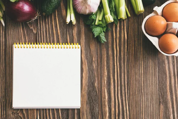 Verse biologische voeding, verse groenten. Sla, komkommer, selderij, ui, eieren en peterselie op houten achtergrond met Kopieer ruimte en Kladblok — Stockfoto