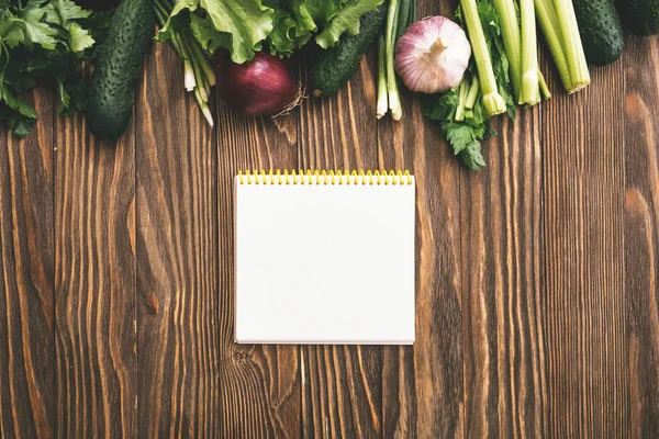 Verse biologische voeding, verse groenten. Sla, komkommer, selderij, ui en peterselie op houten achtergrond met Kopieer ruimte en Kladblok — Stockfoto