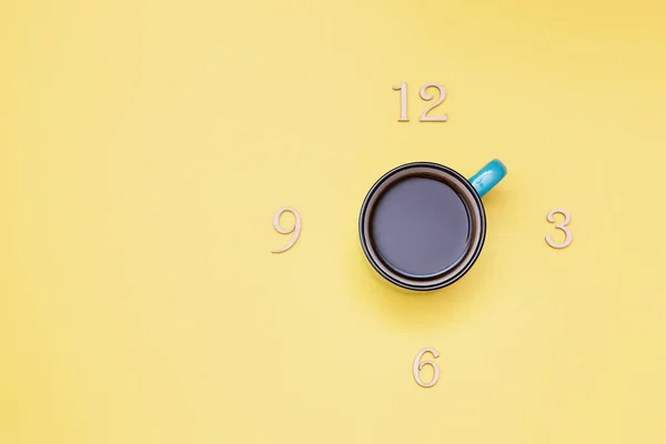 Black coffee and time alphabet letters clock 3 6 9 12 break ceramic blue Cup top view height plan on yellow background — Stock Photo, Image