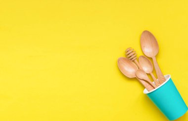 Masa takımı ahşap kaşıklar kağıttan bir fincanda sarı arka plan, üst manzara. Sıfır atık, çevre dostu kavram.