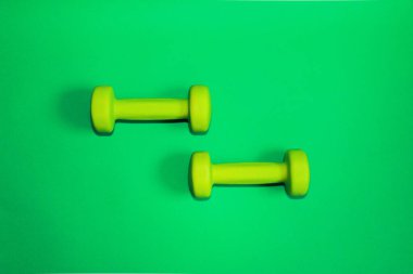 Yeşil arkaplanda yeşil halterler var. Düz konsept fitness, spor salonu ve sağlıklı yaşam tarzı. Yukarıdan görünüm ve alanı kopyala.