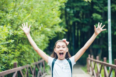 Yaşasın tatiller! Mutlu liseli kız tatilin tadını çıkarıyor. Sırtında beyaz bir tişörtle sokakta dikiliyor..
