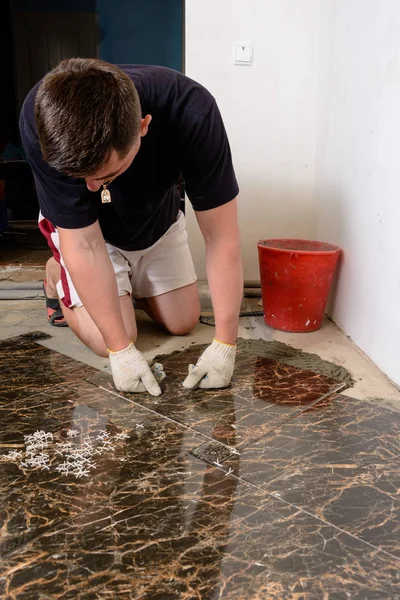 A man places a ceramic tile under pressure over a glue in room of brown color