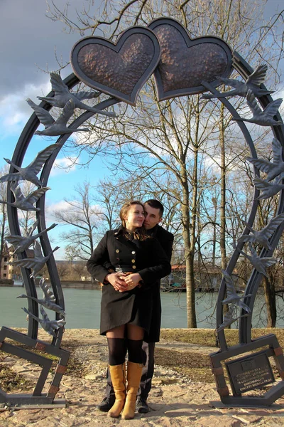 Couple on a bench Harrison Hot SpringsLoving couple in valentines day in a city park against a lake under a large forged heart — Stock Photo, Image