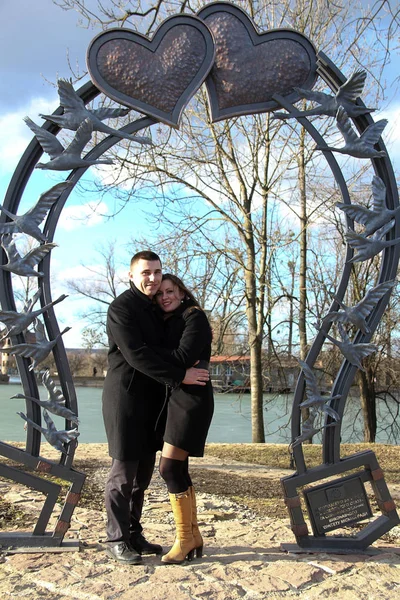 Couple sur un banc Harrison Hot SpringsCouple amoureux dans la Saint-Valentin dans un parc de la ville contre un lac sous un grand cœur forgé — Photo