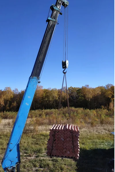 The car crane holds and unloads the brick on the background of the blue autumn sky 2018
