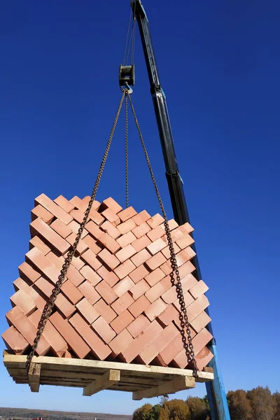 The car crane transfers the brick to the construction site on the background of the sky and field 2018