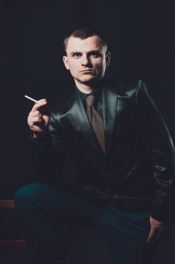 Genç bir adam sigara sigara, siyah bir arka plan, klasik siyah takım elbise 2019
