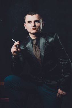 Genç bir adam sigara sigara, siyah bir arka plan, klasik siyah takım elbise 2019