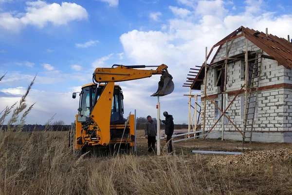 The excavator with a bucket pushes the pillars on the fence in the field near the house 2019