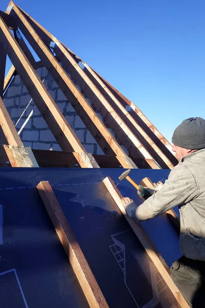 The master nails the bars, fixing this gidrorizer to the rafter, the blue sky appears on the background 2019