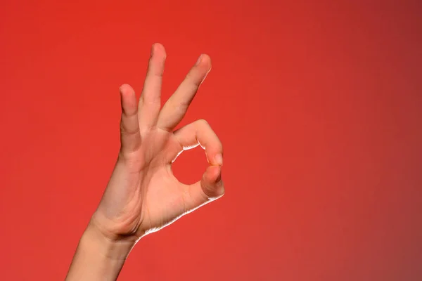 La mano humana muestra el signo ok que simboliza lo positivo, aislado sobre un fondo rojo . — Foto de Stock