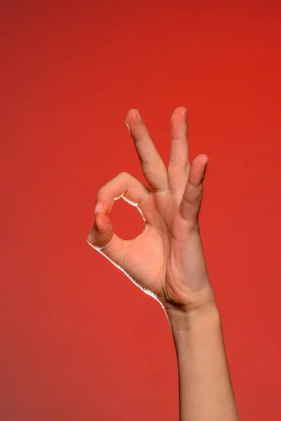 La mano humana muestra el signo ok que simboliza lo positivo, aislado sobre un fondo rojo . — Foto de Stock