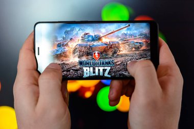 Los Angeles, Kaliforniya, ABD - 9 Mart 2019: adam akıllı telefon yakın çekim elinde tutar ve renkli bir bulanık yan arka plan karşı dünyanın tankları Blitz çalış.