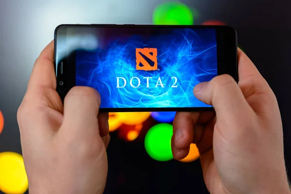 Los angeles, Kalifornien, USA - 9. März 2019: Der Mann hält das Smartphone in Nahaufnahme in der Hand und spielt die Dota 2 vor dem Hintergrund einer farbig verschwommenen Seite. — Stockfoto