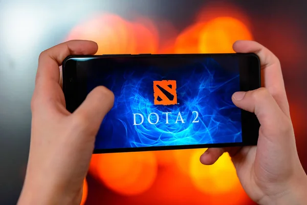 Los angeles, Kalifornien, USA - 9. März 2019: Der Mann hält das Smartphone in Nahaufnahme in der Hand und spielt die Dota 2 vor dem Hintergrund einer farbig verschwommenen Seite. — Stockfoto