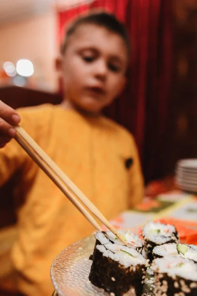 O menino adolescente leva o rolo de sushi do prato para comer — Fotografia de Stock