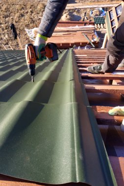 Profesyonel çalışan bir metal kiremit yaprak tarafından bir çatı çatı yüklemesinde çalışır ve bir vida bir matkapla matkaplar