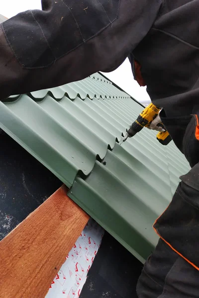 Le travailleur professionnel travaille sur l'installation du toit du toit par les feuilles de la dalle métallique et perce la vis avec la perceuse — Photo