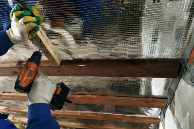 Sihirbaz Akülü matkap kullanır ve sabitleyen vidayı folyo film ve mineral yün Evin çatısı iyileşmek için tutun panoları vida